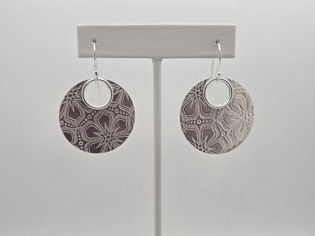Blue Teapot Jewelry sterling silver circular drop earrings with an intricate floral embossed pattern on a display stand